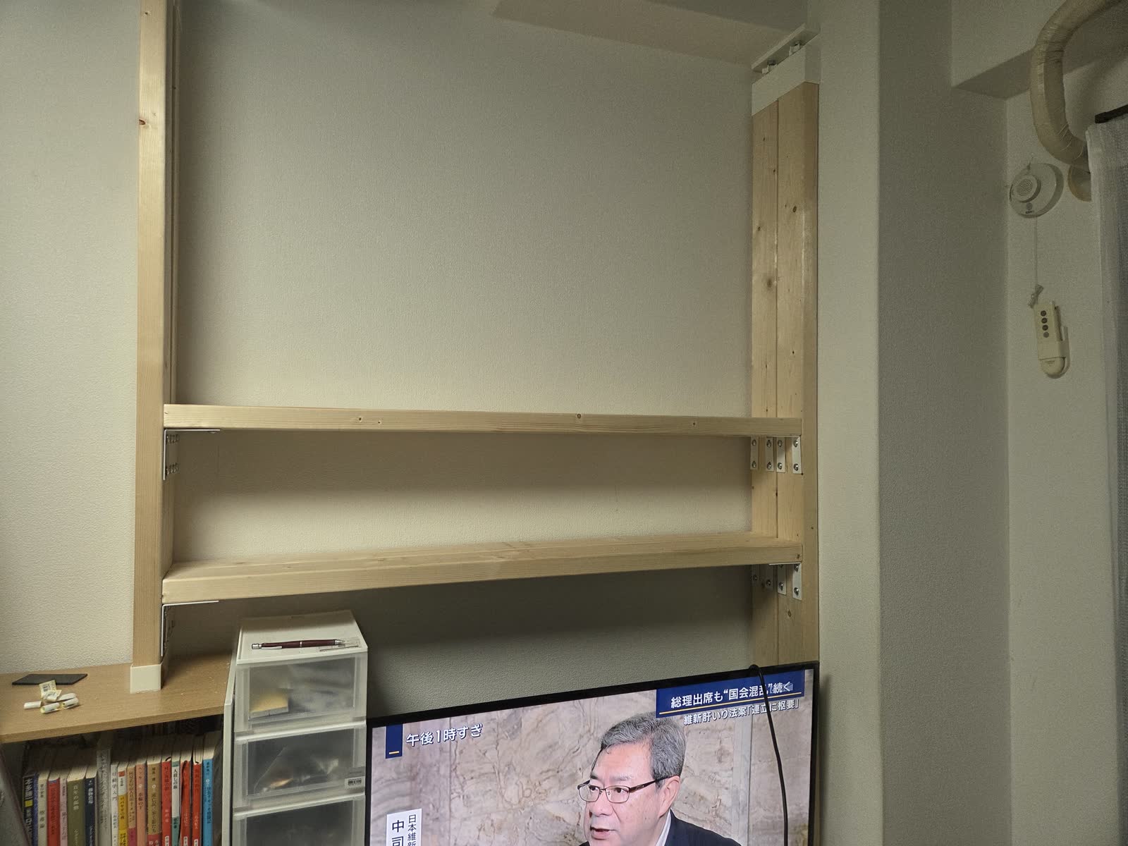 2段目まで組み上がった本棚。テレビの上に棚板が渡り、本が並び始めている。