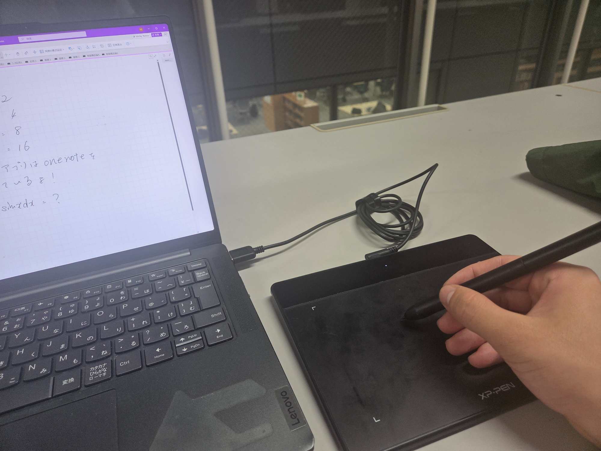 キーボードの隣でペンタブに書き込んでいる手元、PC画面にOneNoteが開いている