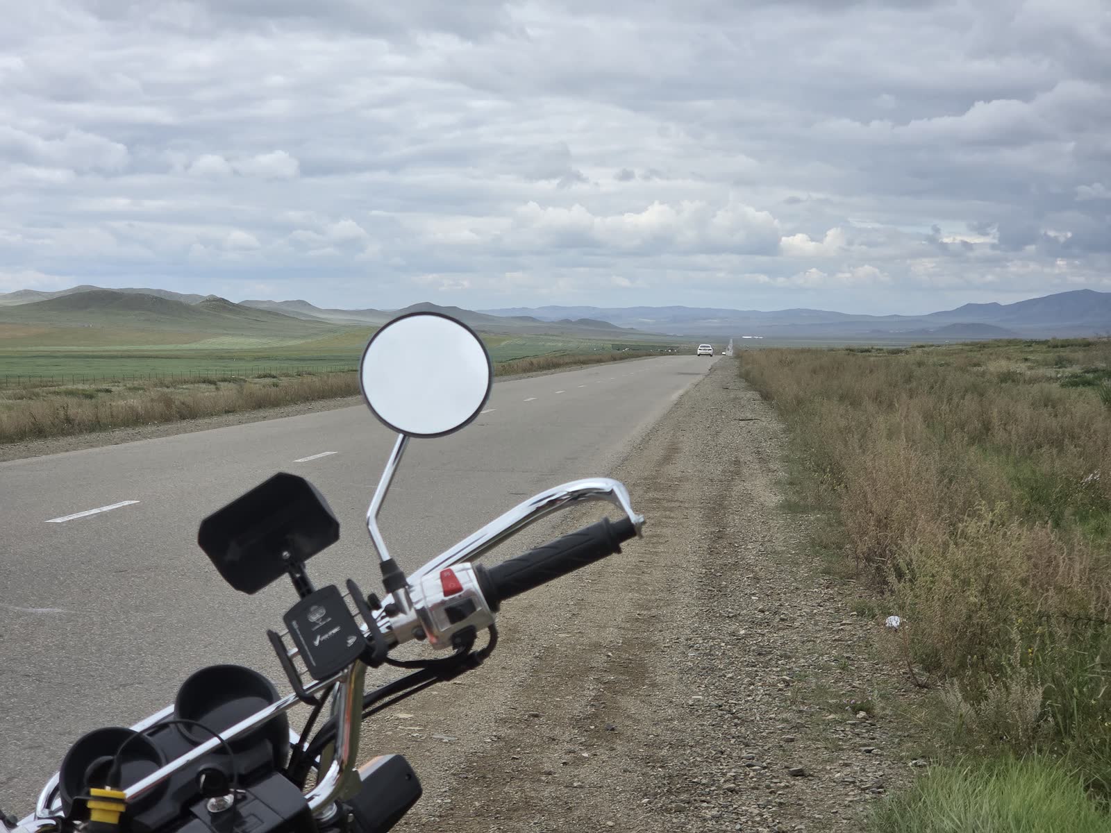 バイクのハンドルの向こうに続く道と丘