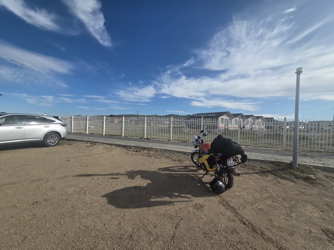 駐車場の隅に止めたバイクと、白い柵の向こうの建物