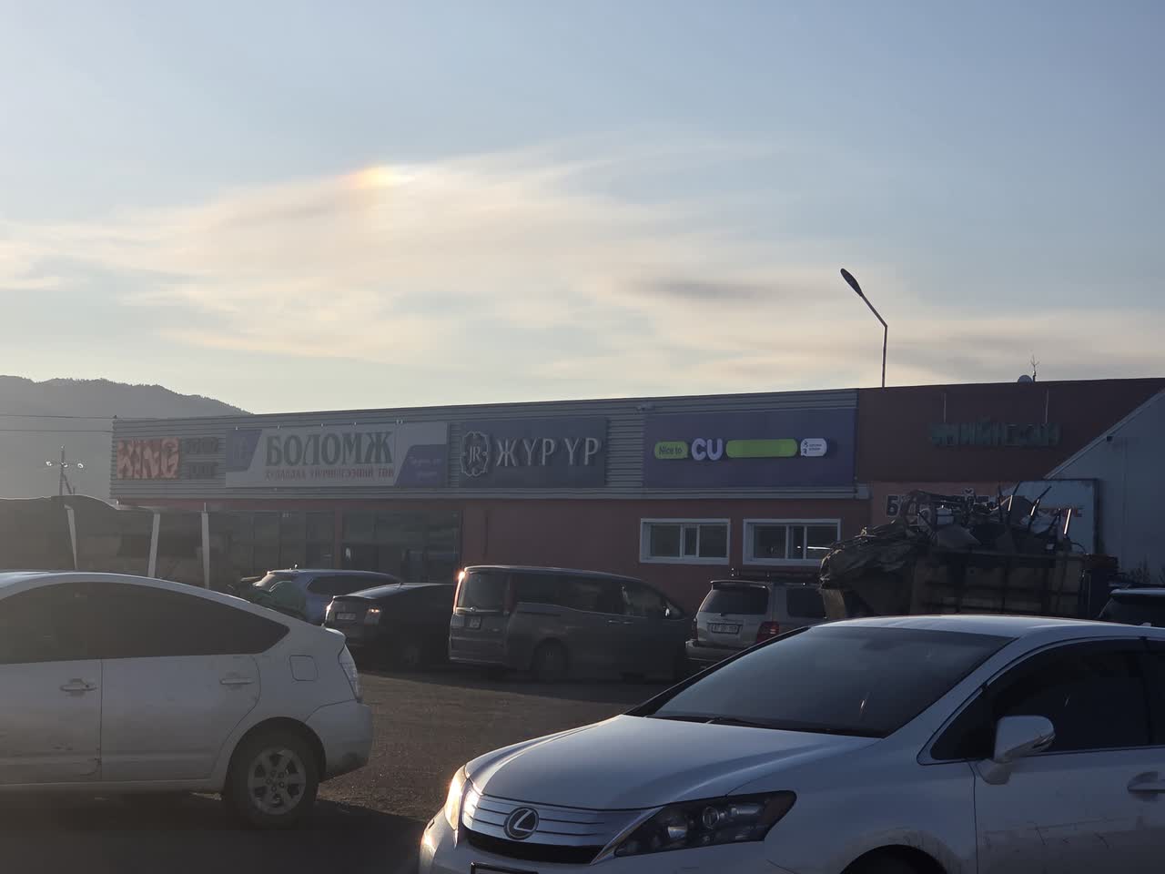 夕方の空の下、同じ建物の別の面に並ぶ店の看板