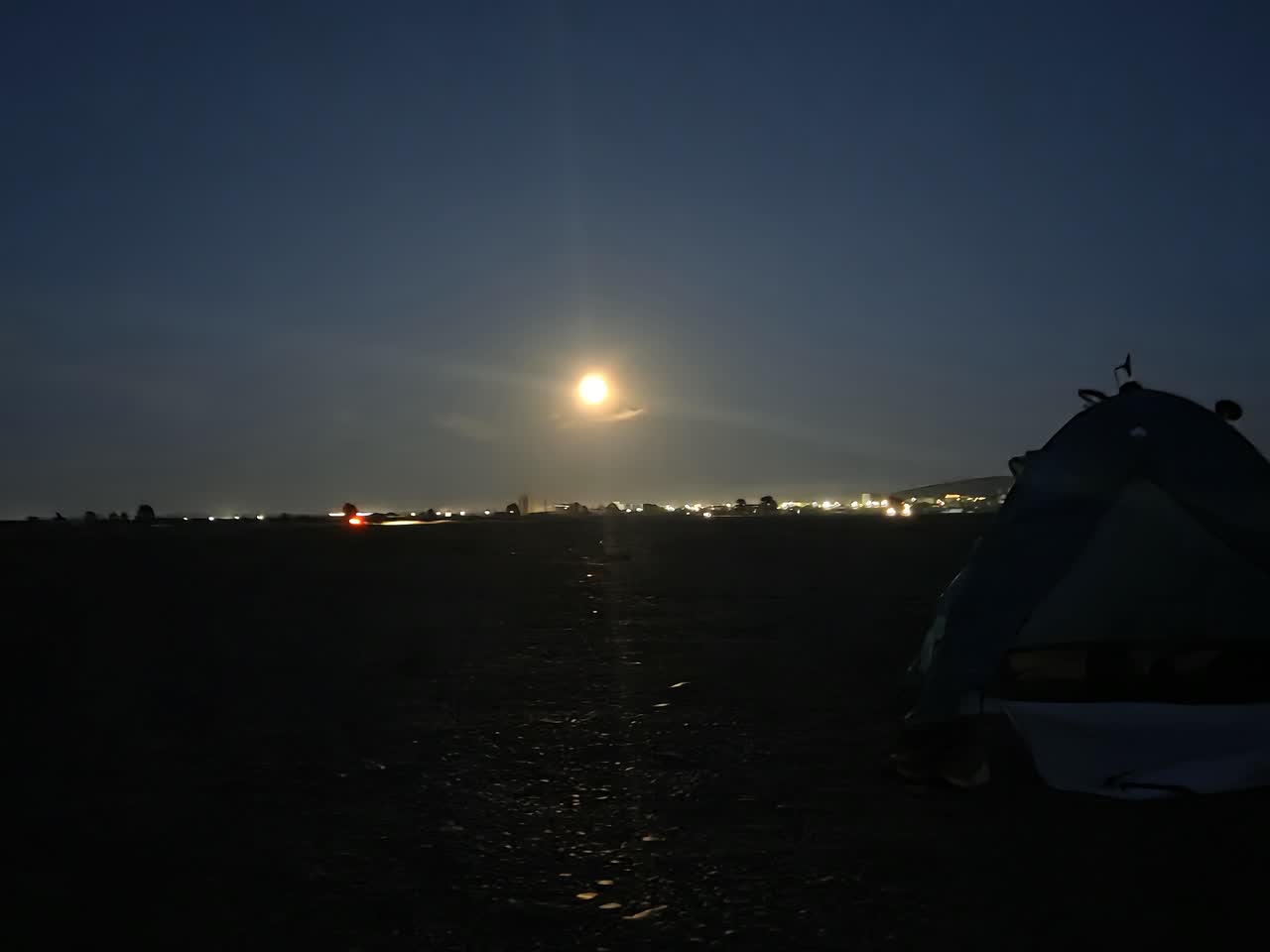 夜の草原に昇る月と、遠くに見える町の明かり