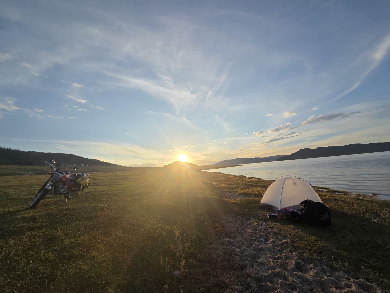夕日に染まる湖畔の草原に止めたバイクと張ったテント